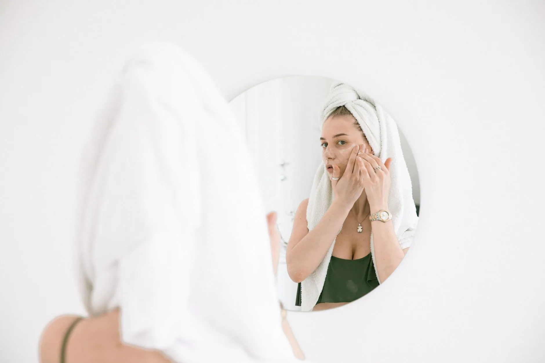 Người phụ nữ thoa kem dưỡng lên vùng gò má trước gương trong phòng tắm.