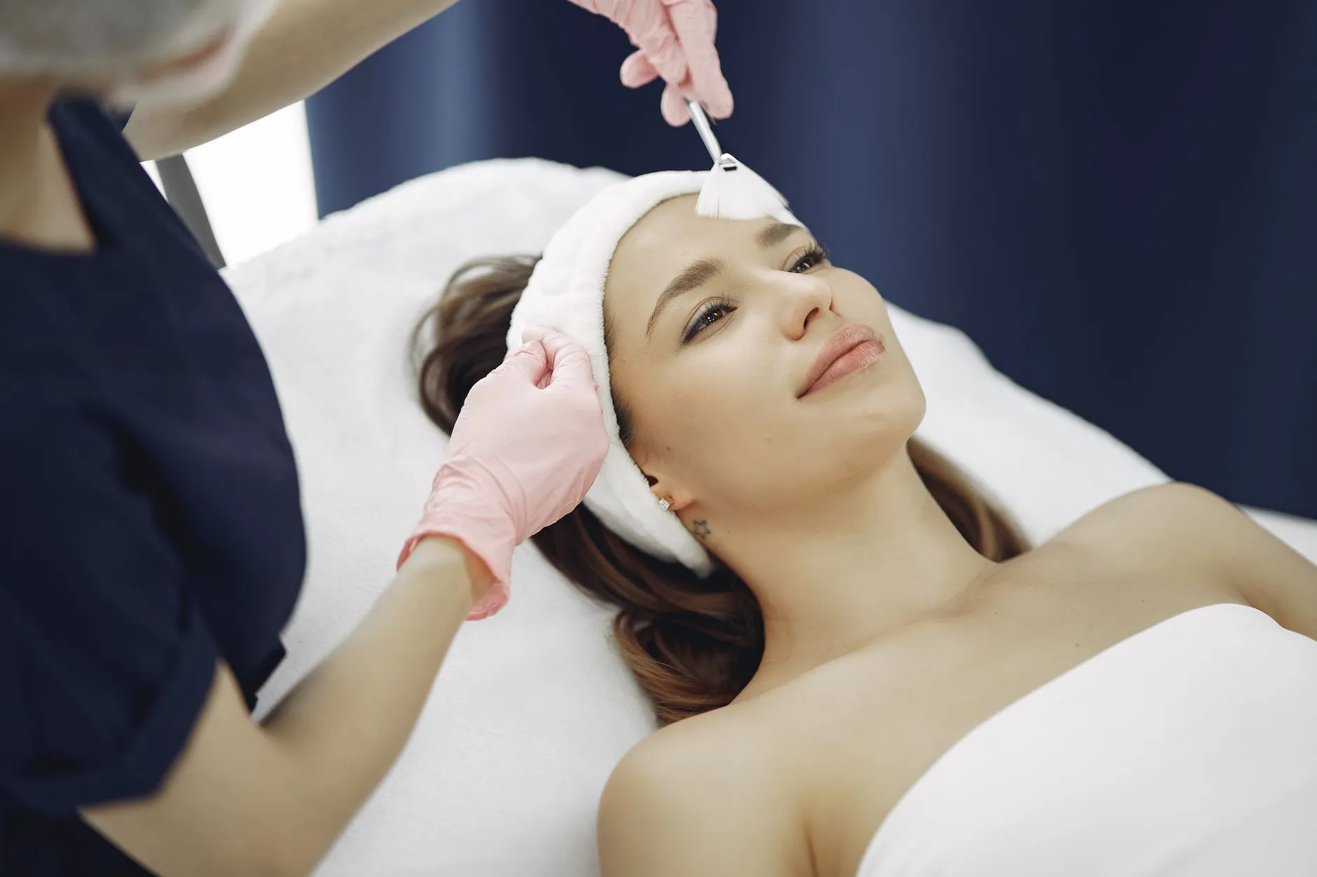 Người phụ nữ nằm trên giường điều trị, nhân viên y tế đang thoa dung dịch lên vùng da mặt.