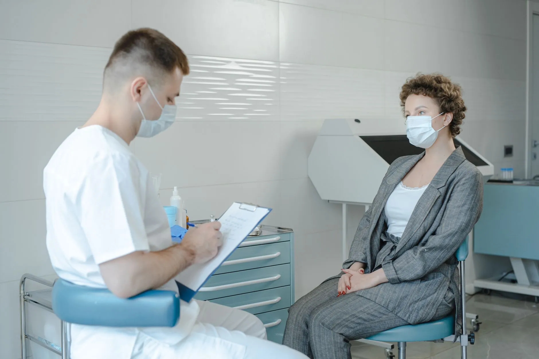 Nhân viên y tế đeo khẩu trang ghi chép trong khi trao đổi với người bệnh tại phòng khám.
