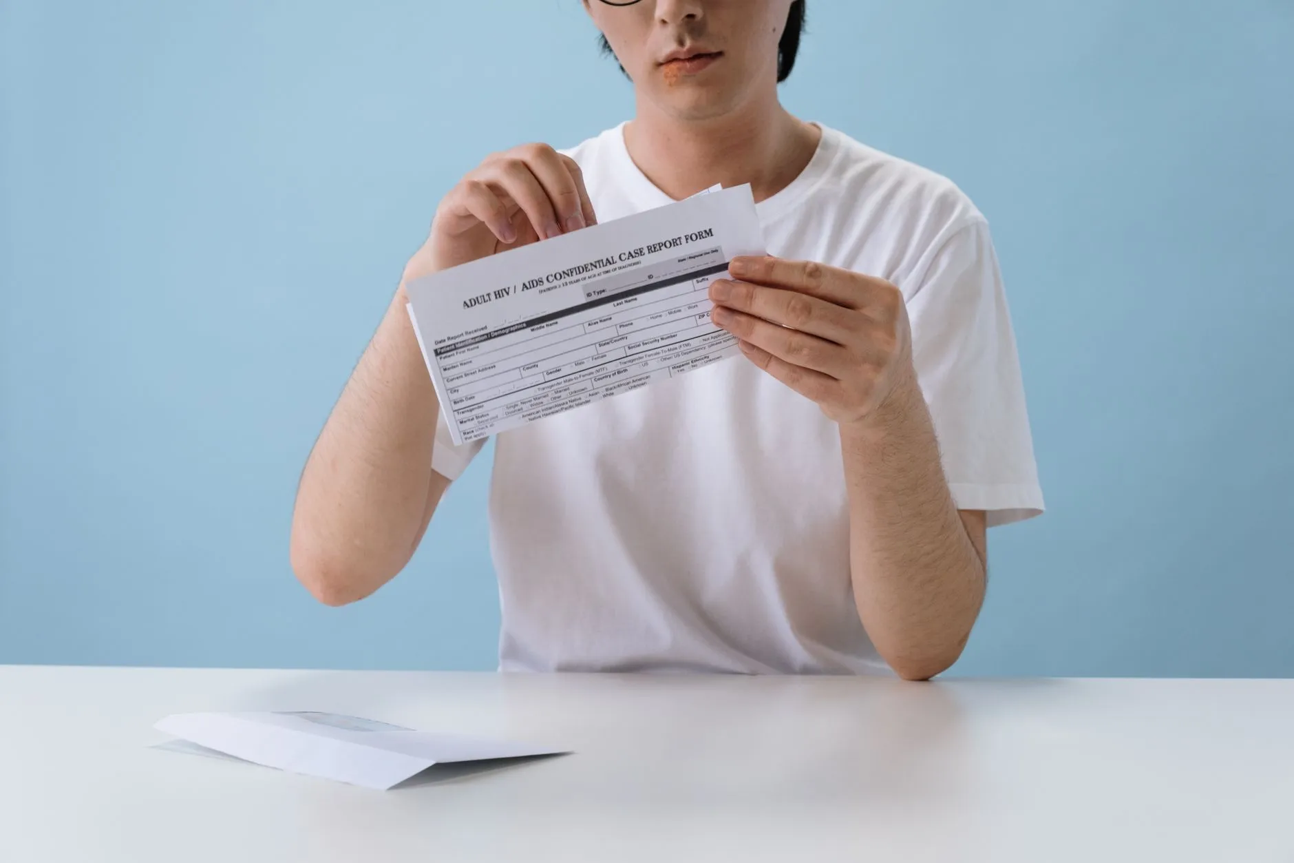 Một người phụ nữ ngồi xem tờ phiếu kết quả xét nghiệm máu bên bàn.