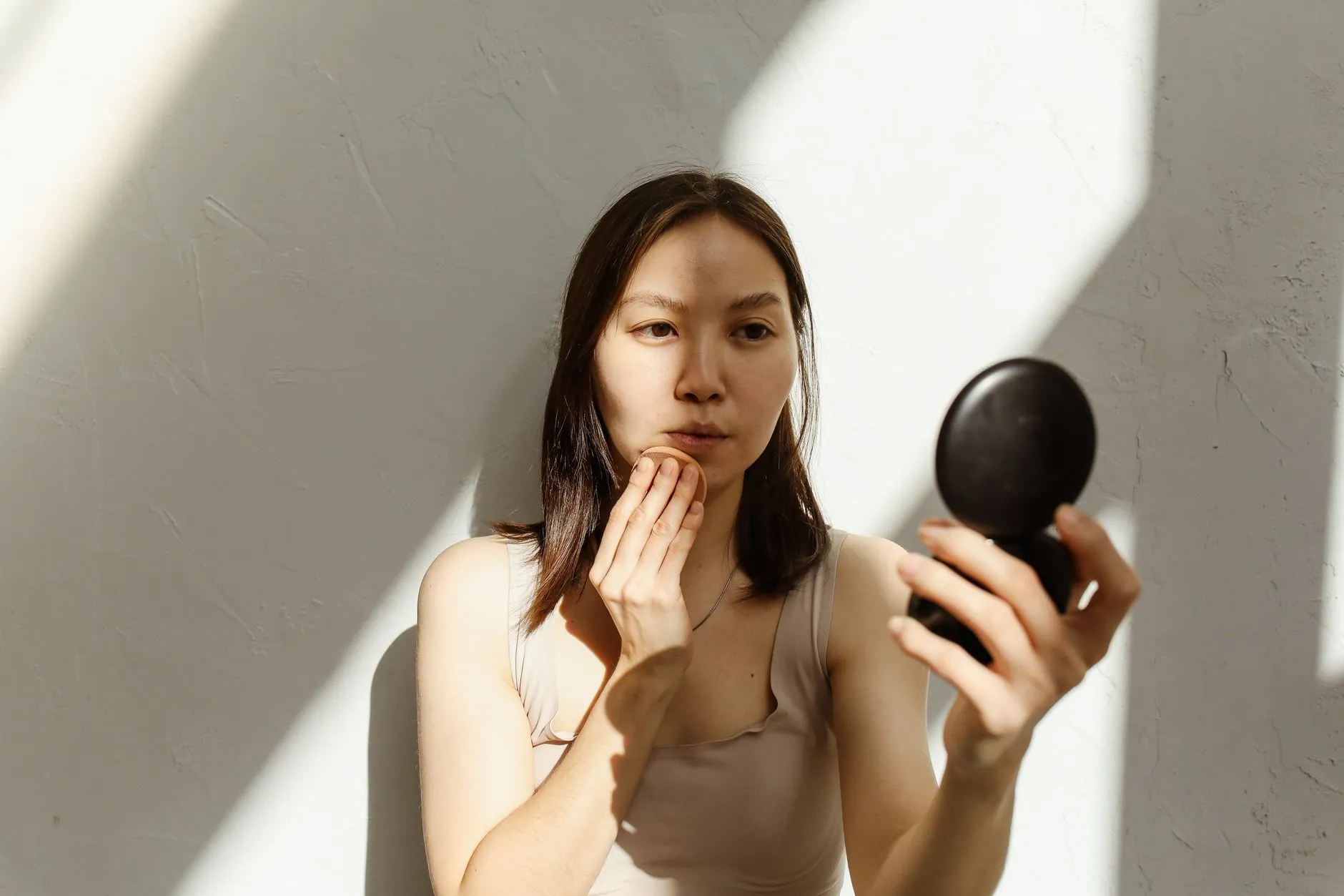 Một phụ nữ trẻ soi gương quan sát vùng cằm và hai bên hàm.