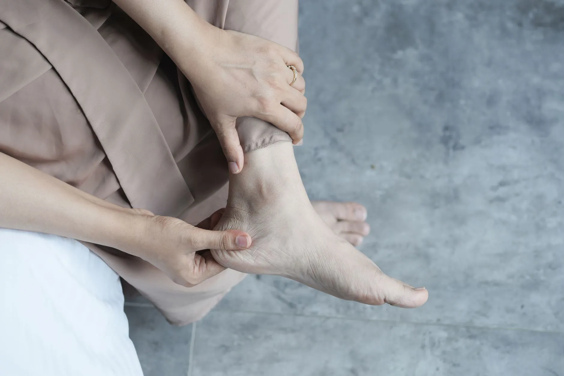 Một người lớn tuổi ngồi xoa nhẹ vùng cẳng chân và cổ chân bên dưới.