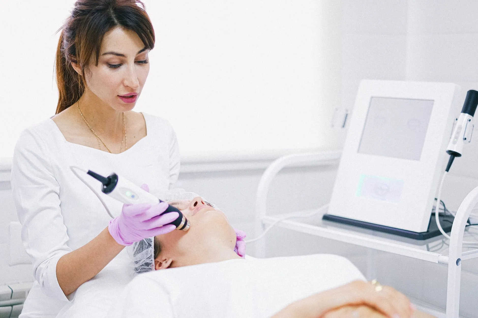 Nhân viên y tế thao tác bằng thiết bị cầm tay trên vùng da mặt của một người bệnh đang nằm tại phòng khám.
