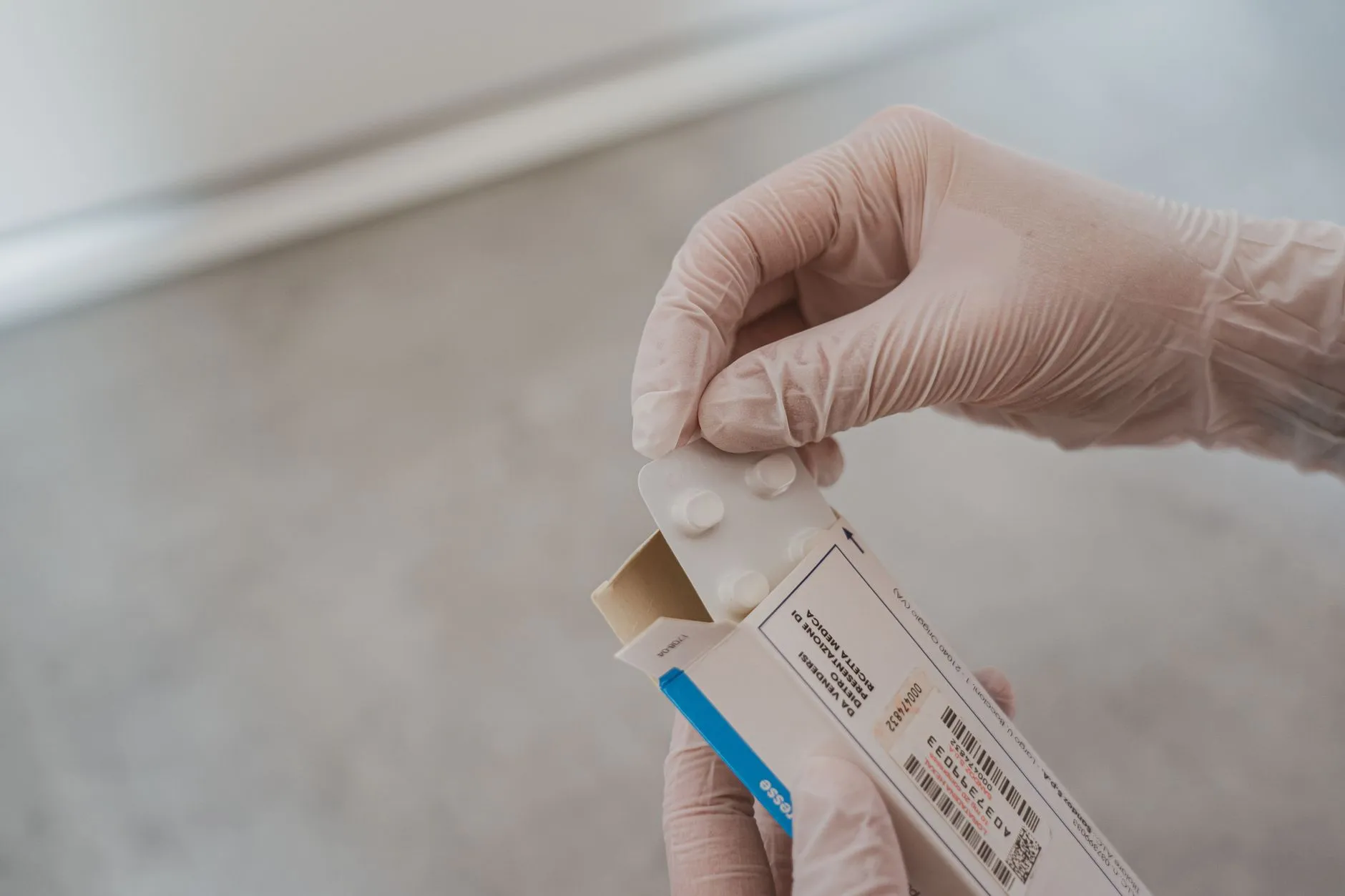 Người phụ nữ cầm vỉ thuốc và xem tờ hướng dẫn bên bàn trong ánh sáng tự nhiên.