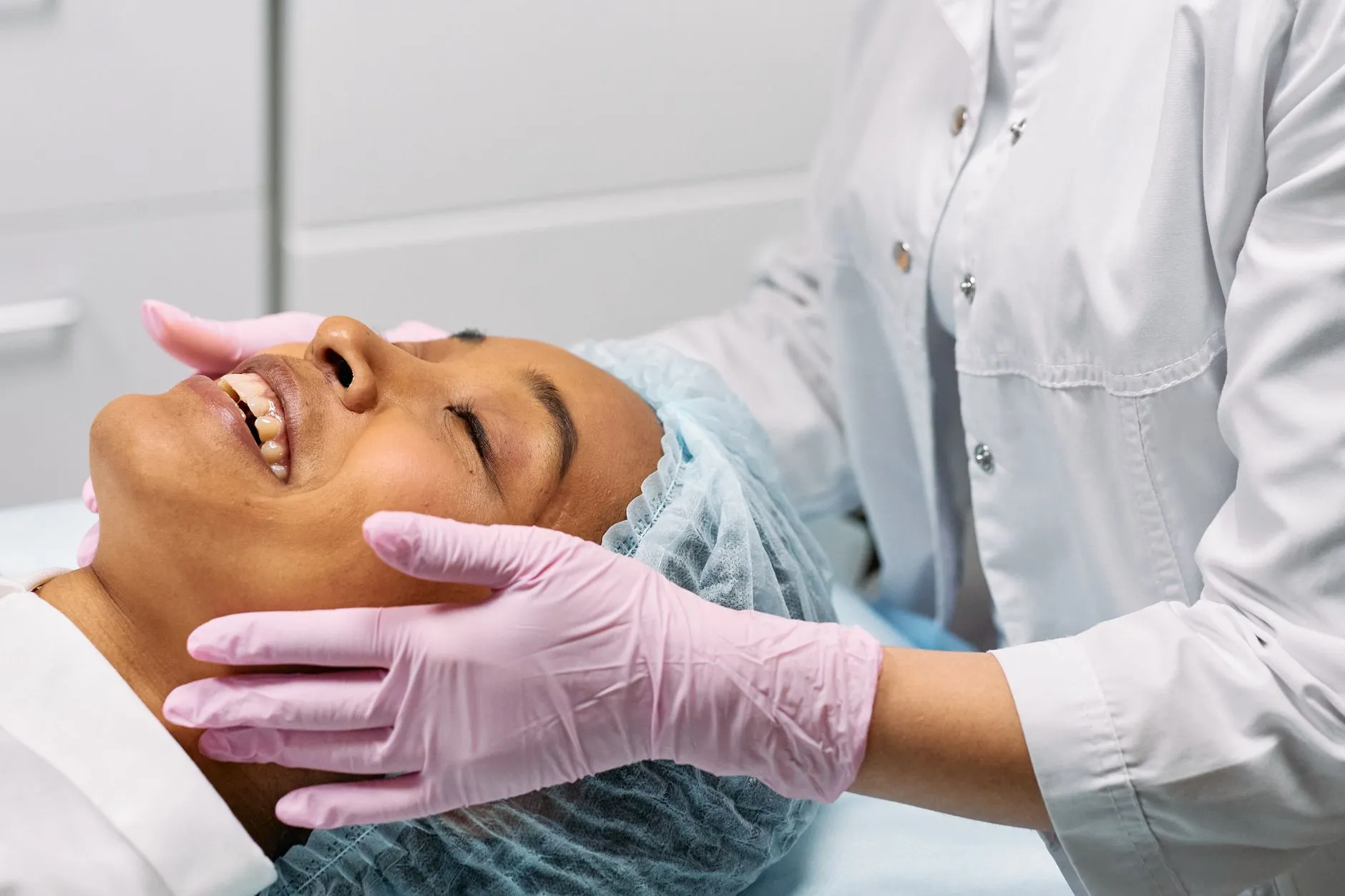 Nhân viên y tế đeo găng chăm sóc da mặt cho người bệnh đang nằm tại phòng khám.
