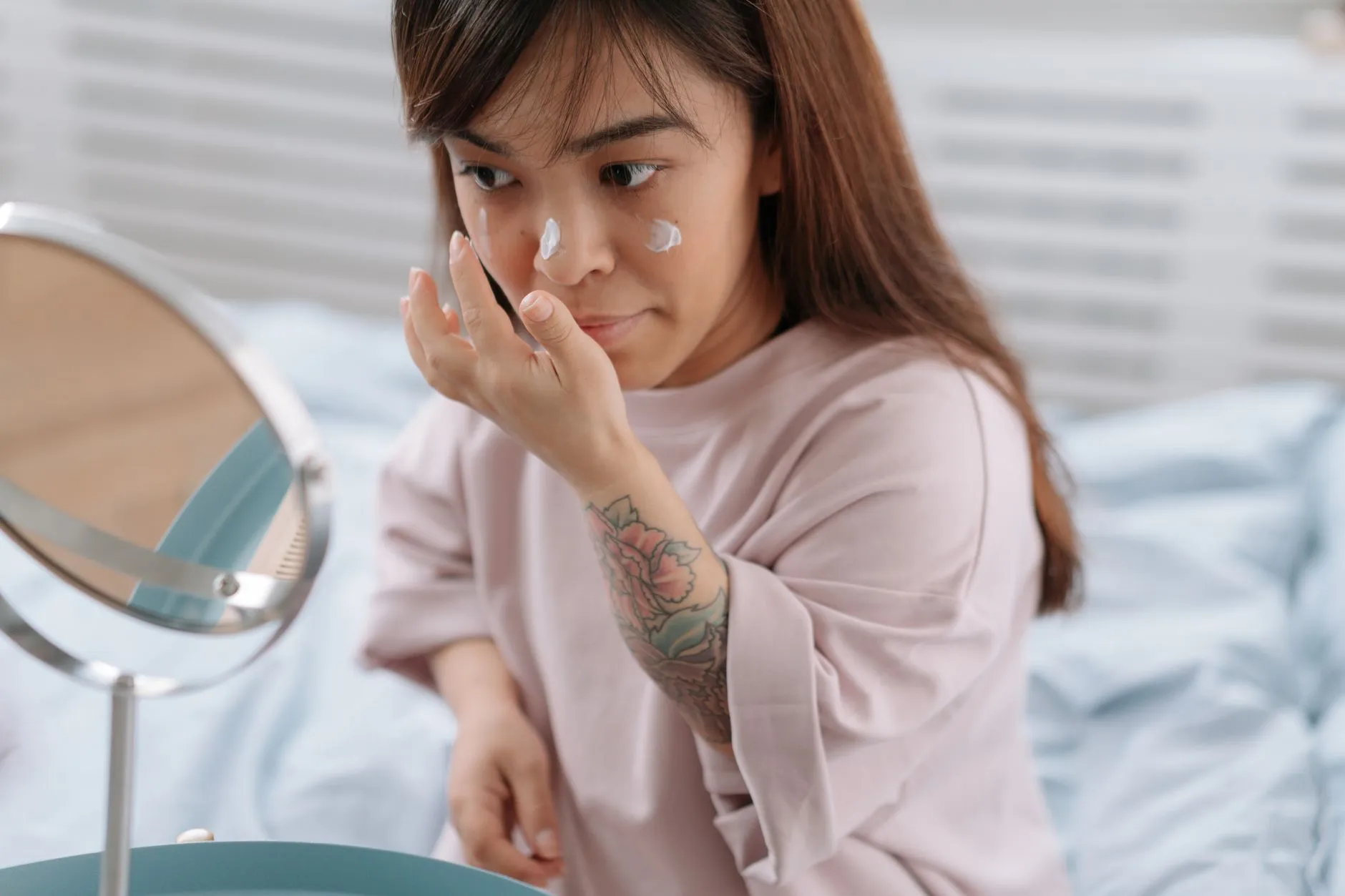 Người phụ nữ ngồi trước gương, thoa kem dưỡng lên vùng má.
