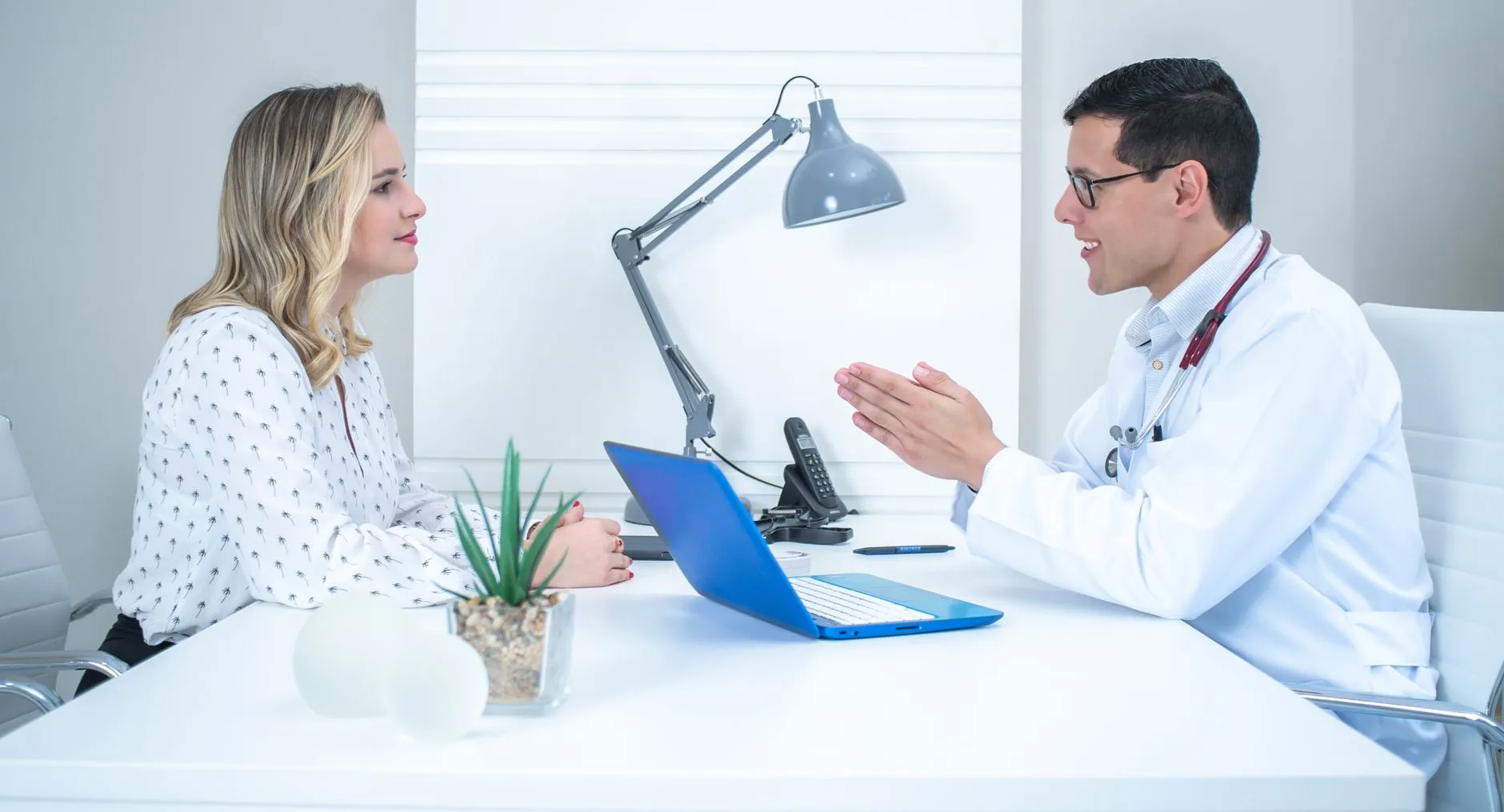 Bác sĩ trao đổi với một bệnh nhân nữ trẻ bên bàn khám trong phòng khám.