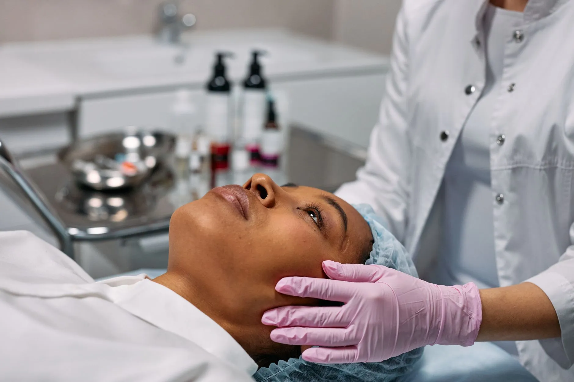 Nhân viên y tế đeo găng tay khám vùng má cho người bệnh nằm trên giường thủ thuật.